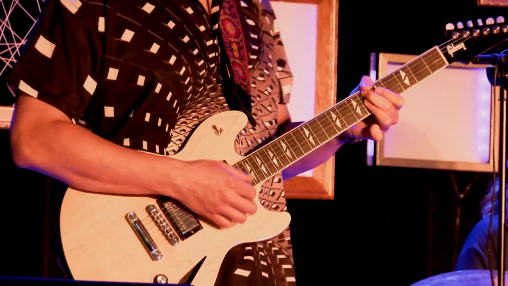 Mike Loce playing electric guitar at a blue-lit concert